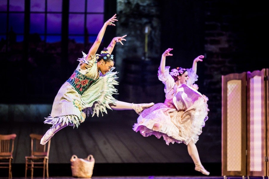 Two ballet dancers dressed in garishly bright colors leap threateningly into the air. 