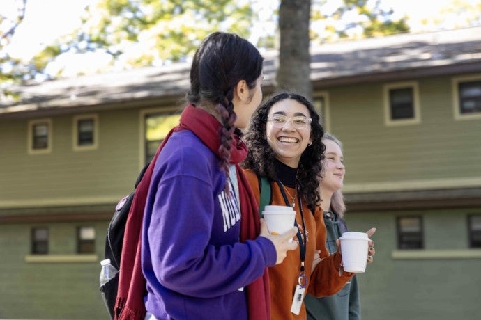 Smiling students stroll on campus with coffees in their hands.