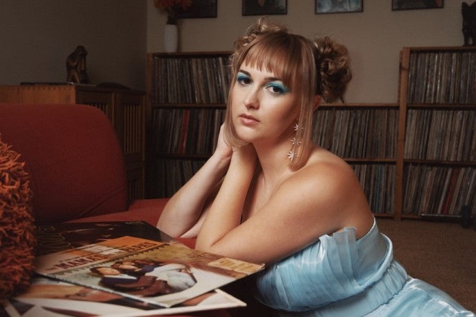 A singer in a light blue dress leans on her hands as she looks into the camera.