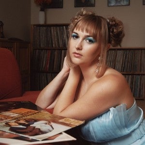A singer in a light blue dress leans on her hands as she looks into the camera.