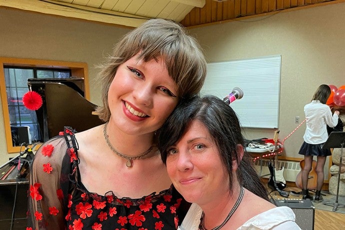 A student in a black and red top stands smiling with her arm around her smiling teacher, who is wearing a white shirt.