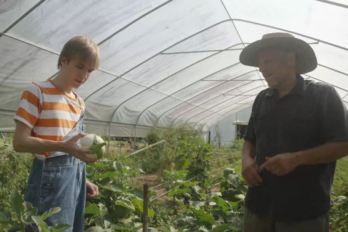 A film student talks with a farmer in a hoop house.