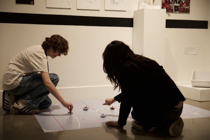 Two students play with spinning tops on the floor.
