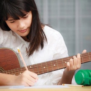 A girl jots down notes while playing guitar