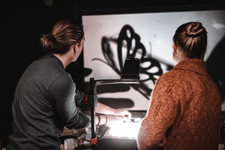 An Interdisciplinary Arts student operates a butterfly-shaped shadow puppet as Alexandra Herryman watches. 