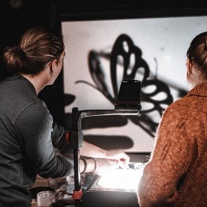 An Interdisciplinary Arts student operates a butterfly-shaped shadow puppet as Alexandra Herryman watches. 