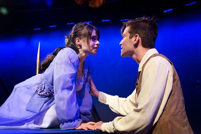 a young man stands at a balcony in front of a young woman