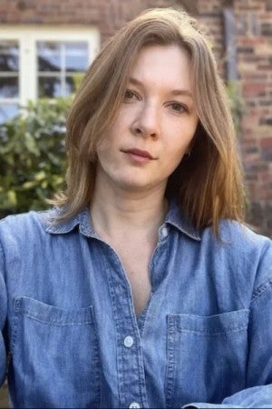 A blonde-haired woman wearing a blue shirt gazes at the viewer.