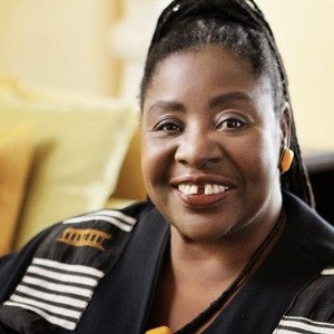 A dark-skinned woman wearing a white and black shirt smiles at the viewer.