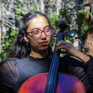 Meena Karimi wears black attire while she performs in the woods.