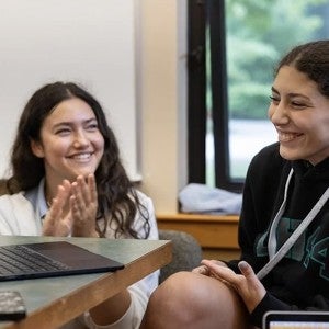 Two students laugh and clap during a writing workshop.