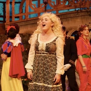 A blonde-wigged girl sings joyfully onstage.