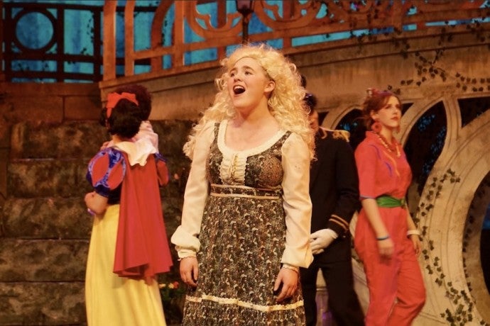 A blonde-wigged girl sings joyfully onstage.