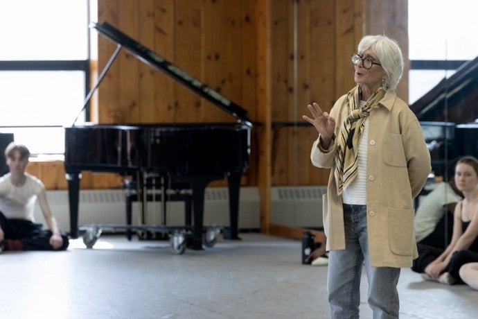 An elderly woman, stylishly dressed, teaches a class of dance students.