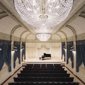 Shot of a stunning, chandelier-hung recital hall with a piano onstage.