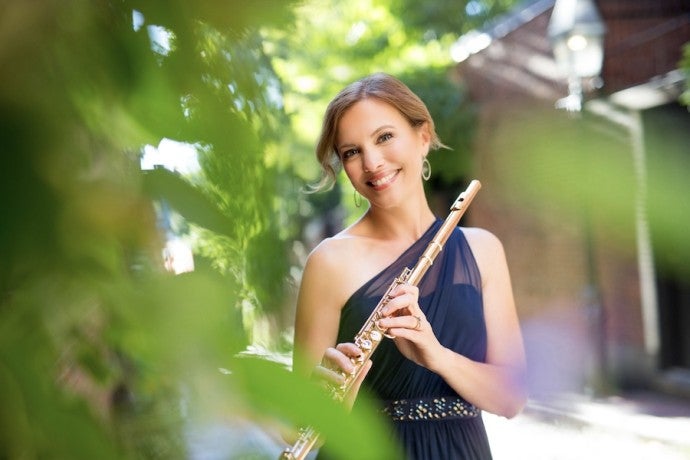 Stagnitta, dressed in dark blue and carrying a flute, smiles into the camera.