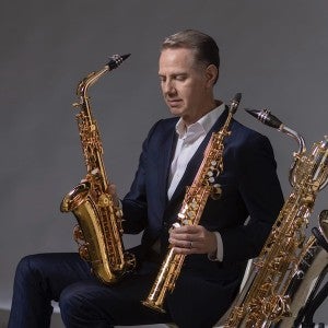 Tim McAllister poses in formal dresswear with three different saxophones.
