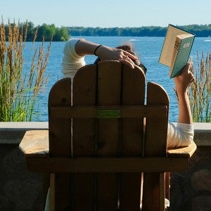 A person reads a book in an Adirondack chair by Green Lake